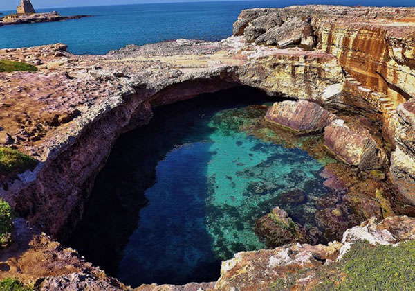 Ingresso della grotta che sfocia in mare aperto con sullo sfondo una torre costiera. Splendida immagine della Grotta della Poesia, Roca Vecchia, Lecce.