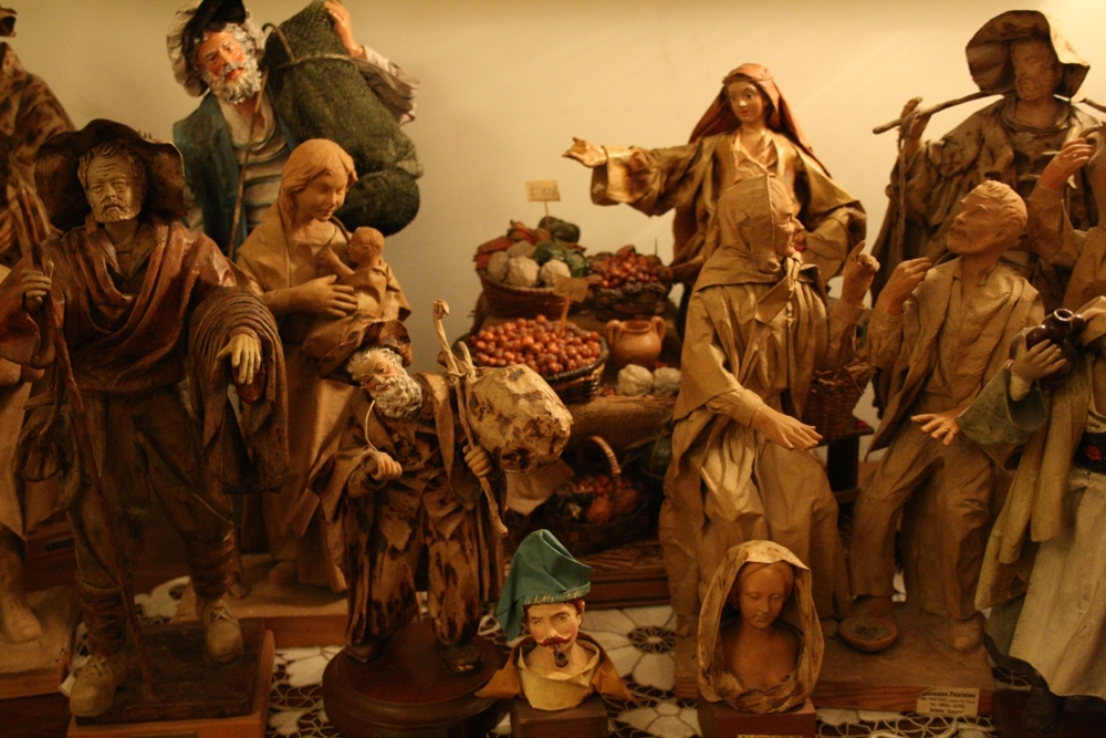 Composizione di diverse statuette in cartapesta vicino ad un tavolino con della frutta.
