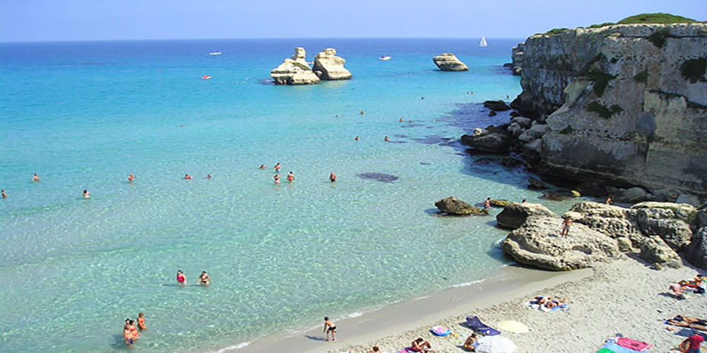 Mare cristallino, la spiaggia e sullo sfondo gli scogli delle "Due Sorelle", a "Torre dell'Orso", Melendugno, Lecce.